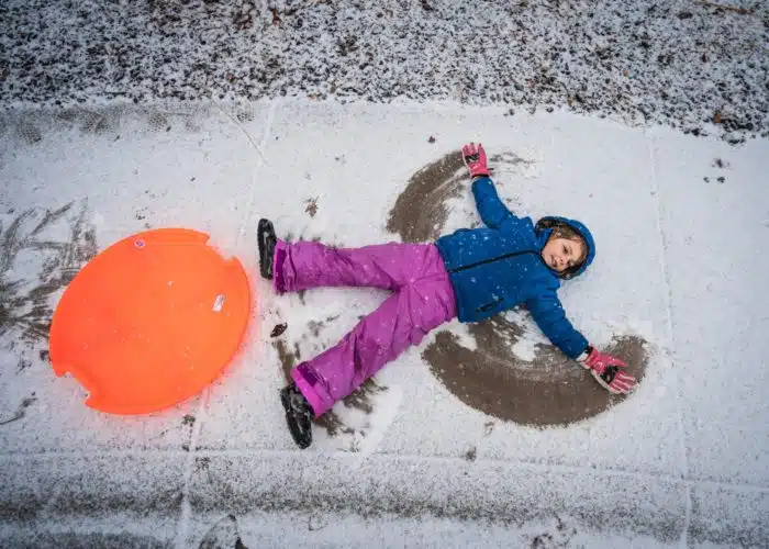 Barn gör en snöängel, jämte ligger en orange pulka