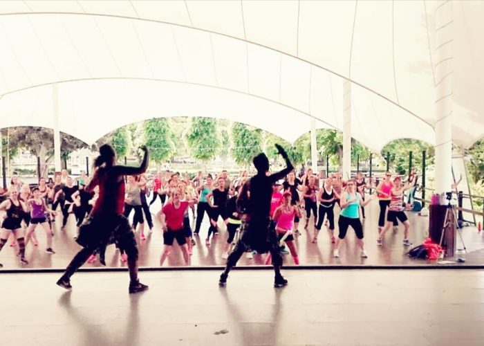Dansinstruktörer dansar zumba på en scen med många deltagare framför sig