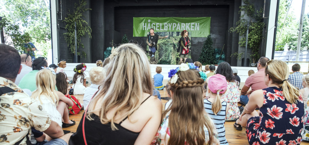 Publik med barn och vuxna tittar på barnteater utomhus