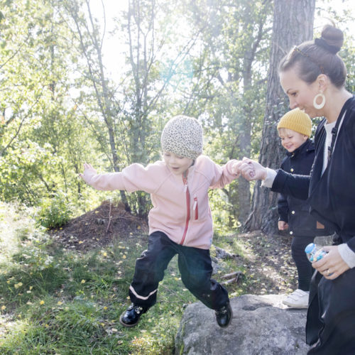 Barn och mammor hoppar och leker längs en stig i skogen