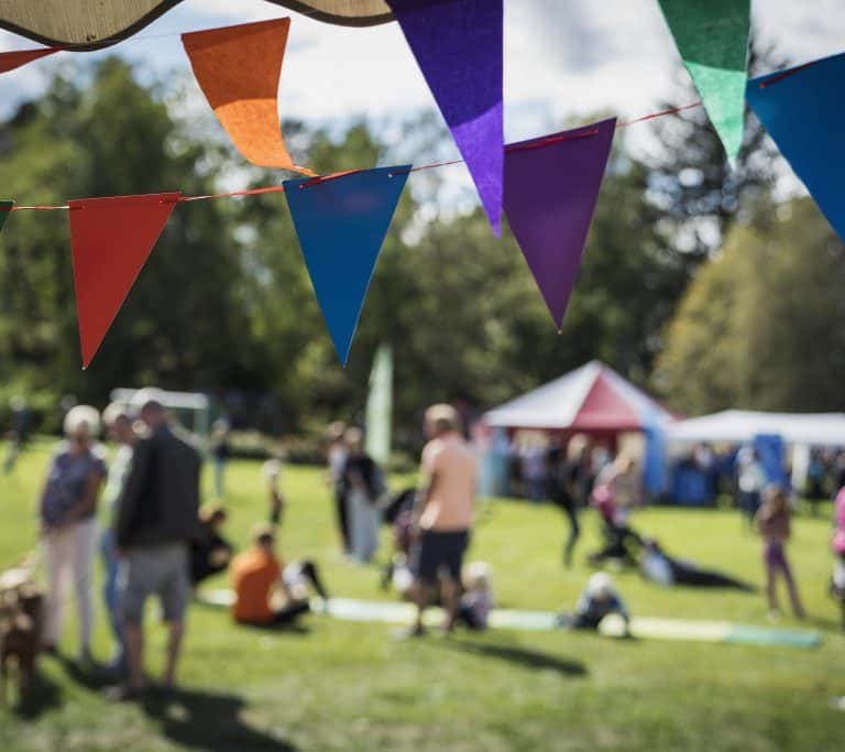 Färgglada vimplar i fokus, i bakgrunden människor i rörelse som sitter och går